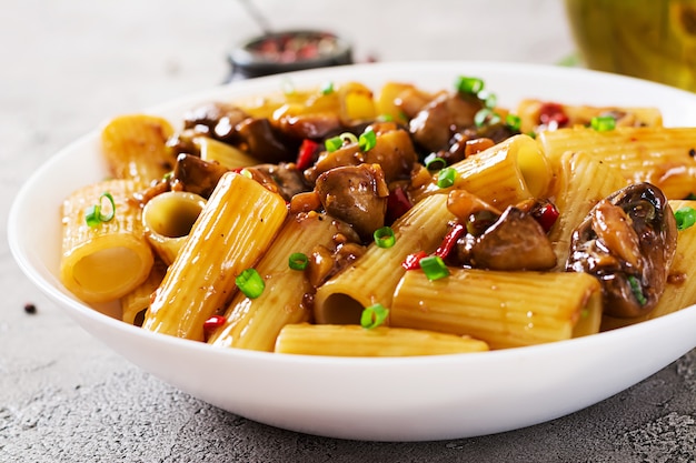 Rigatoni de pâtes végétariennes aux champignons et piments dans un bol blanc sur une table grise. Nourriture végétalienne.