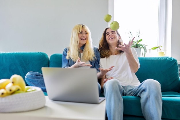 Rire couple d'adolescents s'amusant assis sur un canapé en regardant un ordinateur portable