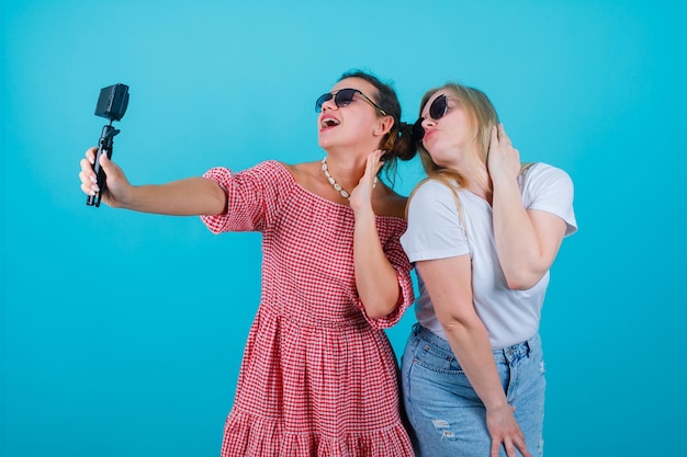 Rire deux filles prennent selfie avec leur mini caméra en se tenant la main sur le cou sur fond bleu