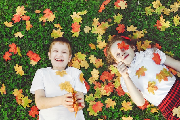 Rire des enfants allongés dans l&#39;herbe jetant les feuilles d&#39;automne dans l&#39;air et montrant les pouces vers le haut.