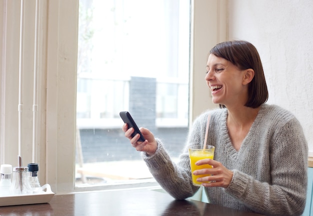 Rire femme assise au café avec téléphone portable