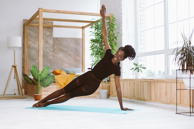 Rire femme multiculturelle souriante faire des exercices de yoga sur tapis Pratiquer la planche latérale Vasisthasana avec un bras à l'intérieur