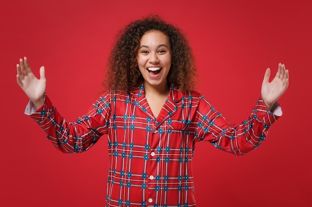 Rire fille afro-américaine en pyjama homewear reposant à la maison isolée sur fond de mur rouge. Détendez-vous le concept de mode de vie de bonne humeur. Maquette de l'espace de copie. Démonstration de la taille avec un espace de travail horizontal.