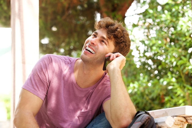 Rire homme assis avec sac à dos et téléphone portable dans le parc