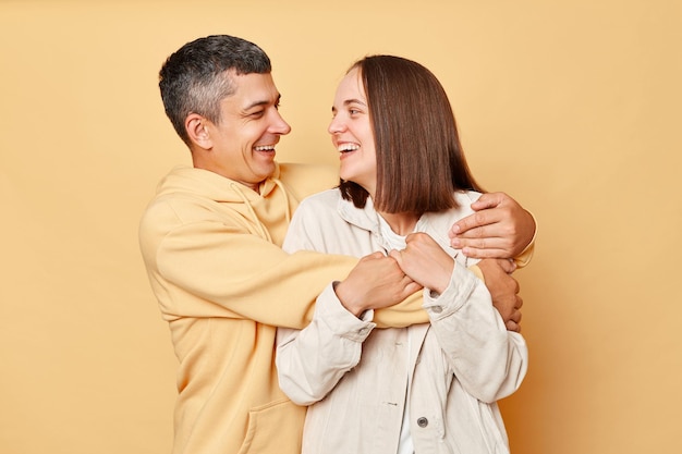 Rire jeune couple souriant debout serrant les uns les autres regardant avec des sourires charmants exprimant l'amour et la pose douce isolée sur fond beige