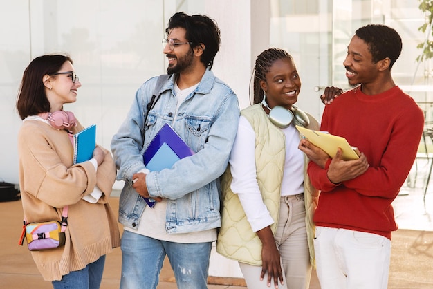 Rire de jeunes étudiants de diverses personnes en casual avec des écouteurs, des cahiers communiquent pendant leur temps libre