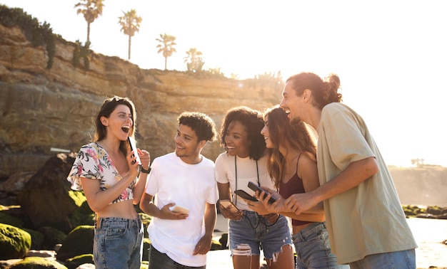 Rire de jeunes internationaux excités avec des smartphones s'amusent ensemble sur la plage