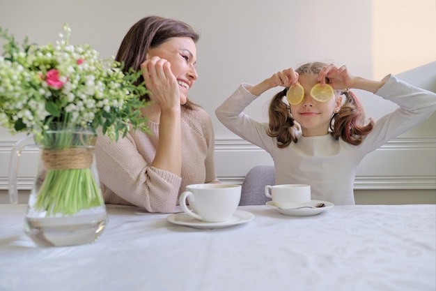 Photo rire mère et fille buvant dans des tasses et mangeant du citron.