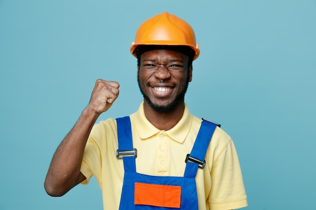 Rire montrant oui geste jeune constructeur afro-américain en uniforme isolé sur fond bleu