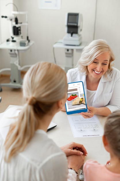 Rire ophtalmologiste positif tournant l'écran de la tablette à son patient