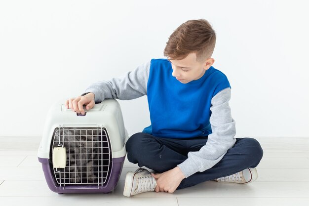 Rire petit garçon positif tient une cage avec un chat scottish fold à côté de lui assis sur le sol dans un nouvel appartement. Concept de protection des animaux de compagnie. Copyspace