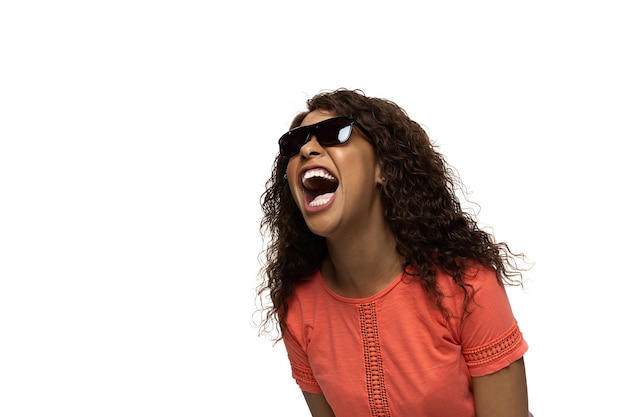 Rire riche. Jeune femme afro-américaine avec des émotions et des gestes populaires drôles et inhabituels sur fond de studio blanc. Émotions humaines, expression faciale, ventes, concept publicitaire. Look tendance inspiré par