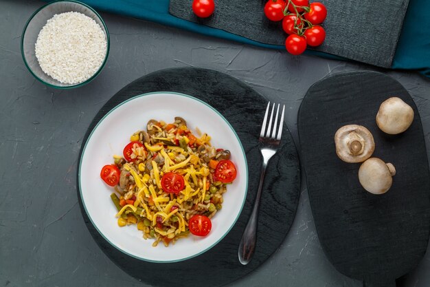 Risotto aux boeufs et fromage dans une assiette sur fond gris près de champignons, tomates et riz sur des tableaux noirs. photo horizontale