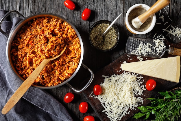 Risotto de boeuf haché dans une marmite en métal avec une cuillère sur une table en bois sombre avec des ingrédients, cuisine italienne, vue horizontale d'en haut, mise à plat