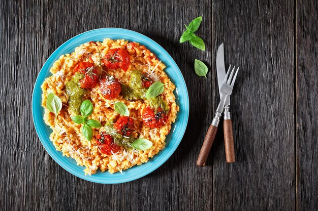 Risotto crémeux aux tomates avec tomates cerises et sauce pesto sur une assiette bleue à plat espace libre