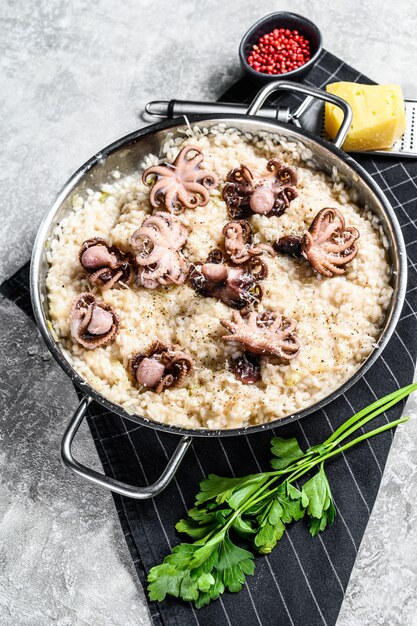 Risotto italien au poulpe et aux champignons décoré de parmesan et de persil. Fond gris. Vue de dessus