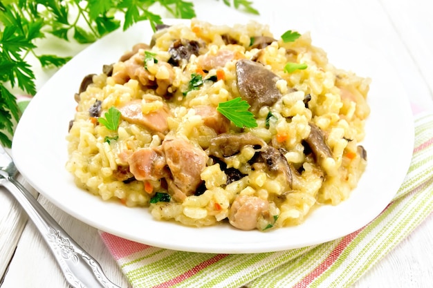 Risotto de riz aux champignons viande de poulet fromage et ail dans une assiette sur une fourchette à serviette et persil sur fond de planche de bois