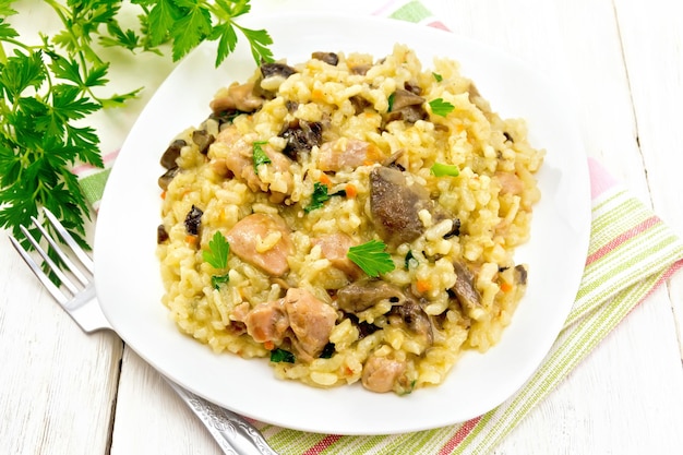 Risotto de riz aux champignons, viande de poulet, fromage et ail dans une assiette sur un torchon, fourchette, persil sur fond de planche de bois