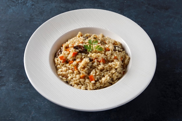 Risotto, riz italien aux champignons, légumes et persil servi sur assiette en porcelaine blanche