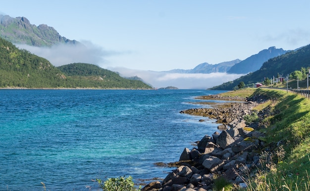 Photo rivage pierreux de la baie bleue contre les montagnes dans le brouillard, lofoten, norvège