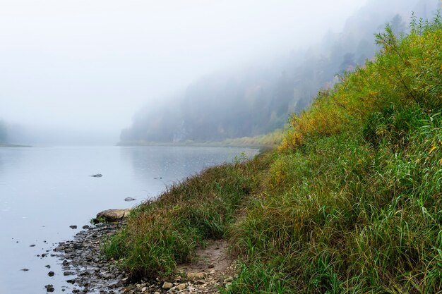 Rivière d'automne avec des rives boisées escarpées dans la brume matinale