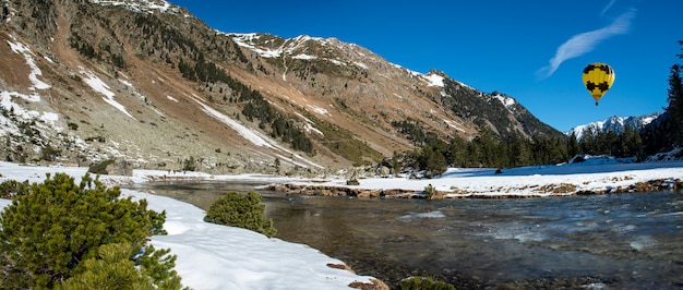 Photo rivière dans les montagnes enneigées des pyrénées avec ballon à air chaud jaune