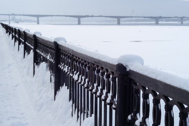 Rivière gelée et clôture de remblai en fonte contre le ciel couvert de neige du soir