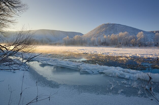 Rivière gelée depuis les berges vallonnées et les gros blocs de glace