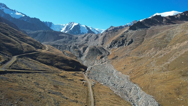 Rivière de montagne avec vue sur les sommets enneigés. Il y a un chemin de terre le long de la rivière.