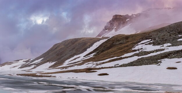 Rivière noyée dans la neige et la glace avec des montagnes en arrière-plan dans les Alpes.