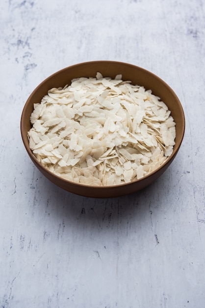 Riz aplati cru ou flocons de riz épais ou minces pour les collations Namkeen Chivda ou Aloo Poha pour le petit-déjeuner indien, servi dans un bol