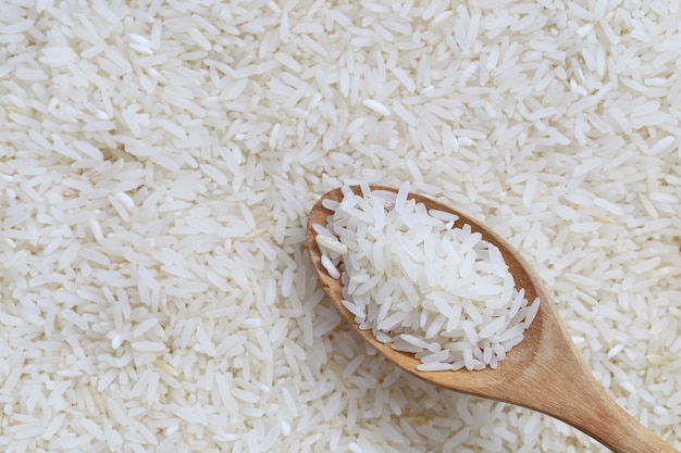 Riz au jasmin dans une cuillère en bois sur fond de riz blanc.