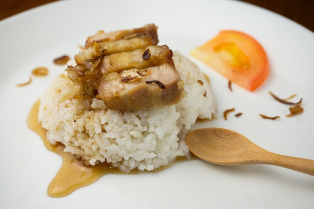 riz au porc grillé dans un plat blanc avec une cuillère en bois sur la table