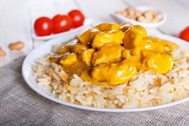 Riz au poulet sauce curry à la noix de cajou sur un fond en bois blanc.