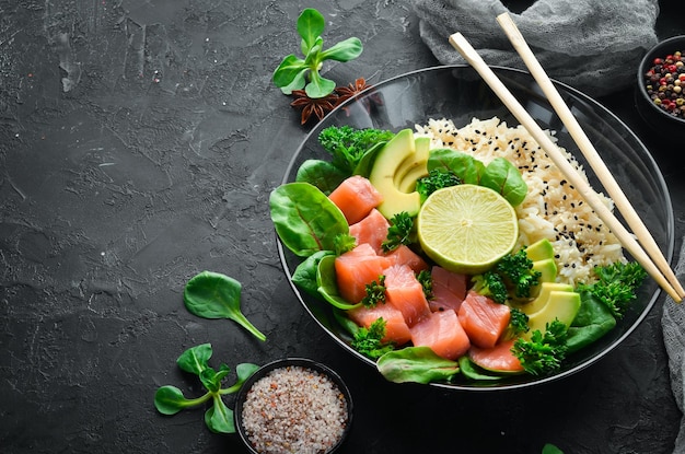 Riz au saumon, avocat et épinards Dans une assiette noire sur un fond en bois Vue de dessus Espace libre pour votre texte Mise à plat