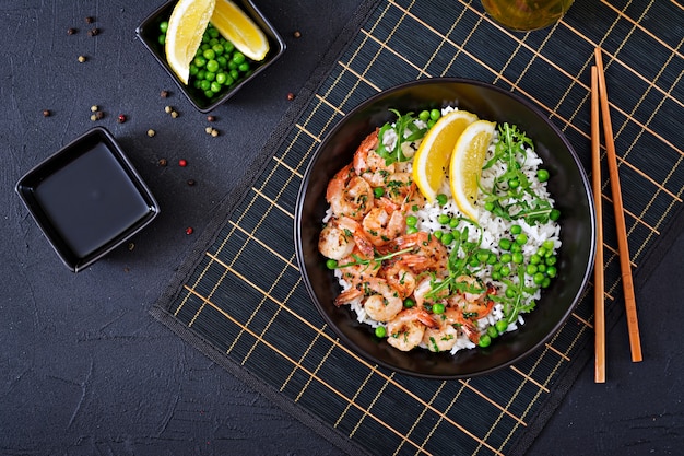 Riz aux jeunes pois verts, crevettes et roquette dans un bol noir. Nourriture saine. Bol de Bouddha. Vue de dessus. Mise à plat