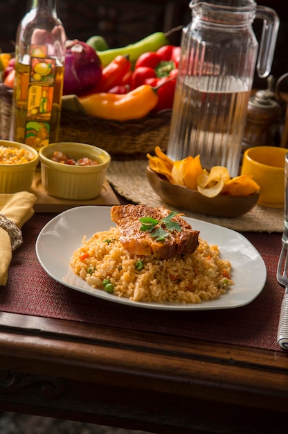 Riz aux légumes avec côtelette de porc Pérou cuisine réconfortante traditionnelle péruvienne mise en place table en bois