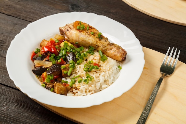 Riz aux légumes et cuisse de poulet sur une planche en bois faite à la main à côté d'une fourchette sur une table en bois