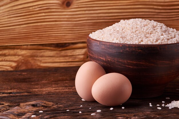 Riz blanc dans un bol en argile sur table et oeufs sur fond de bois.