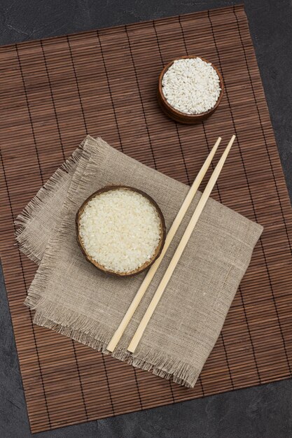 Riz blanc dans un bol en bois. Bâtons de bambou sur serviette. Serviette marron. Mise à plat