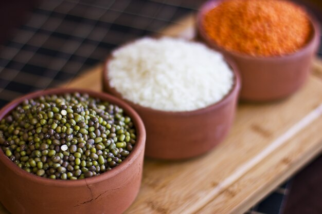 Riz blanc, lentilles rouges et pois verts mache sur un plateau en bois.