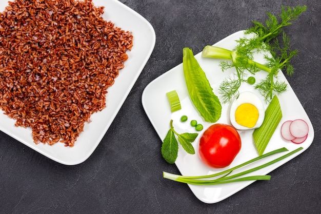 Riz brun dans une assiette blanche La moitié de l'oeuf tomate et herbes dans un bol blanc