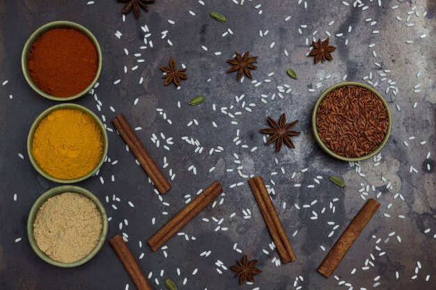 Riz brun rouge dans un bol en céramique verte. Gingembre, curcuma, poivre dans des bols. Bâtonnets d'anis étoilé et de cannelle.