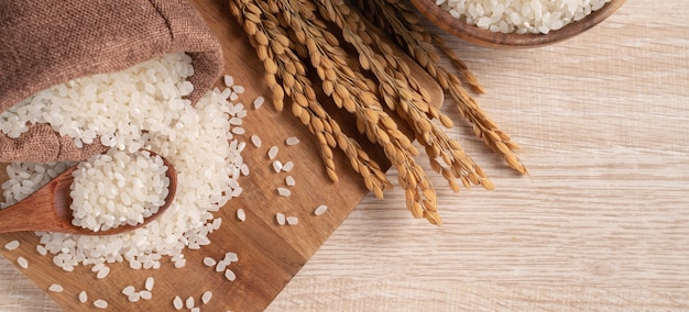 Riz cru blanc dans un bol avec l'oreille sur le fond de la table en bois.