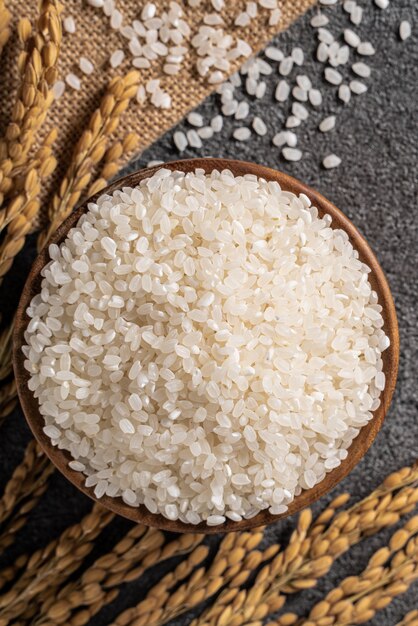 Riz cru blanc dans un bol avec l'oreille sur fond de tableau noir foncé.