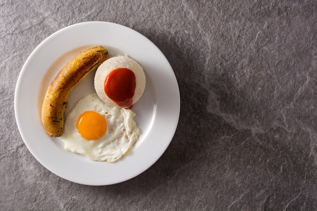 Riz cubain typique avec banane frite et oeuf au plat sur une plaque sur une surface grise