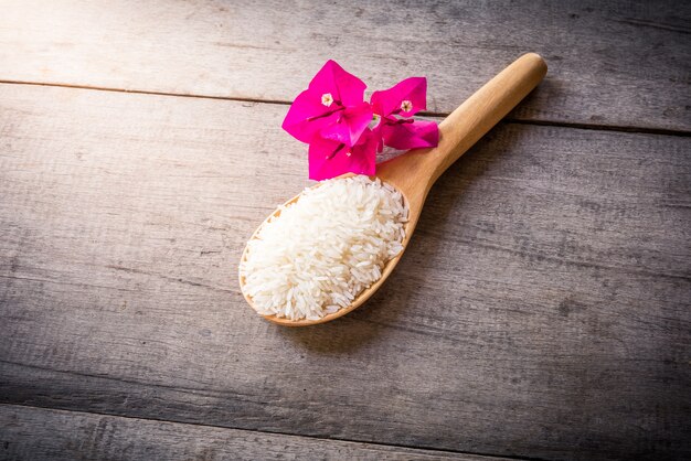 Riz sur cuillères en bois sur fond en bois et fleur rose, nature morte