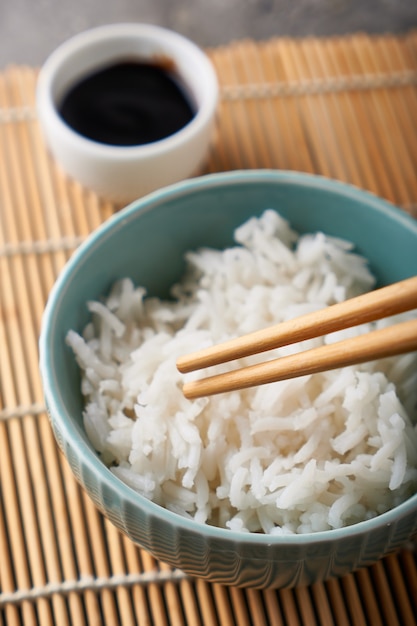 Riz dans un bol en porcelaine, avec des baguettes japonaises, sauce soja, servi sur une table en pierre grise Close up