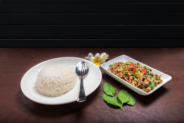 Riz avec du porc frit avec une feuille de basilic dans un plat blanc sur une table brun foncé