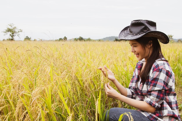 Le riz d'une femme d'affaires prospère regarde le plant de riz doré dans sa main avec le sourire et la fierté